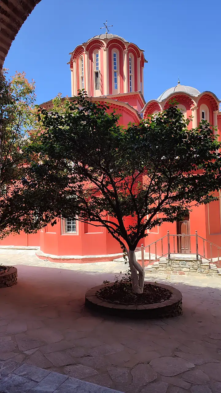 Купол храма монастыря Кутлумуш на Афоне, видимый через арку и деревья во дворе