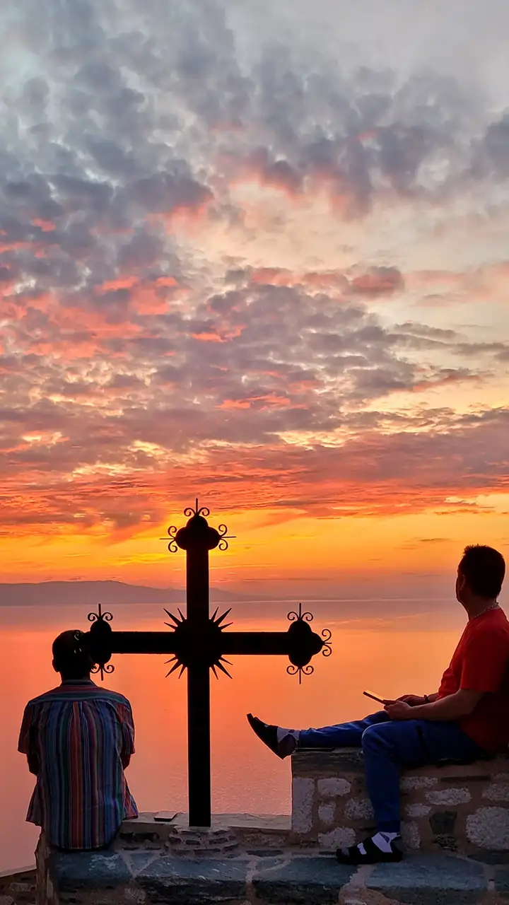 Два паломника сидят у креста в скиту святой Анны на Афоне, любуясь закатом над морем