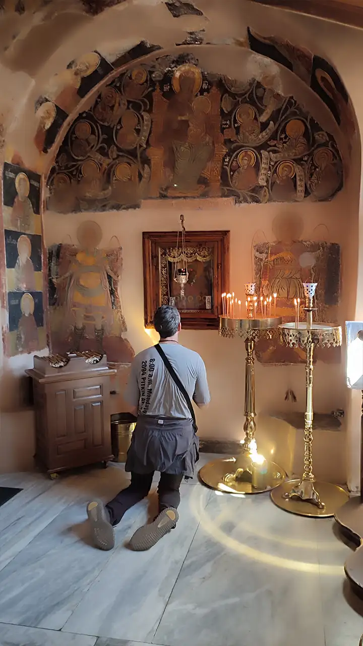 Паломник на коленях молится перед иконой и горящими свечами в монастыре Ксенофонт на Афоне